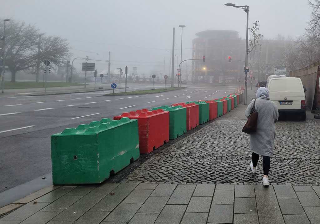 Verregneter Straßenzug, eine Person läuft über den Bürgersteig, der mit großen Blöcken abgesperrt ist