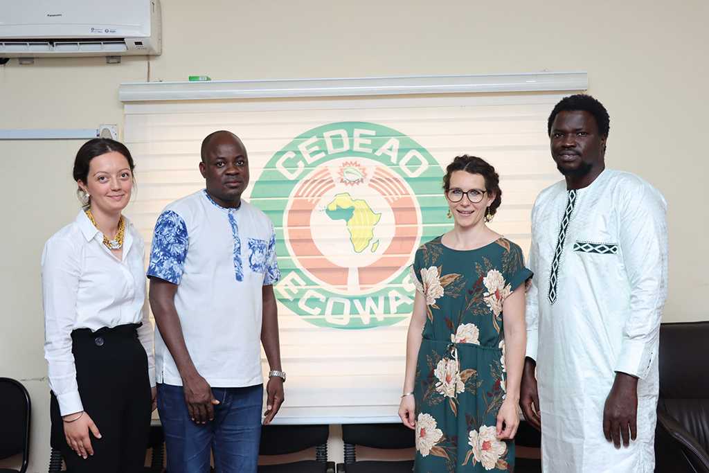 Vier Personen stehen vor einer Leinwand, auf der das Logo der ECOWAS zu sehen ist: eine gelbe Afrika-Karte, bei der die westafrikanischen Staaten grün eingefärbt sind, die von einem roten und einem grünen Ring umschlossen sind, mit der Schrift CEDEAO - ECOWAS.