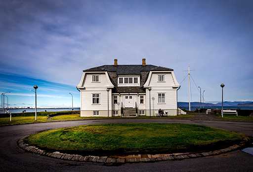 Foto eines weißen Hauses vor blauem Himmel, davor eine Wiese