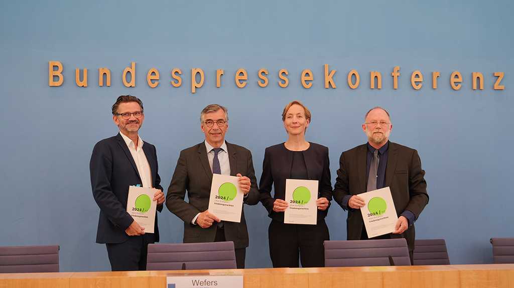 Vier Personen stehen vor einer Wand mit dem Schriftzug Bundespressekonferenz. Sie halten die Ausgabe 2024 in den Händen