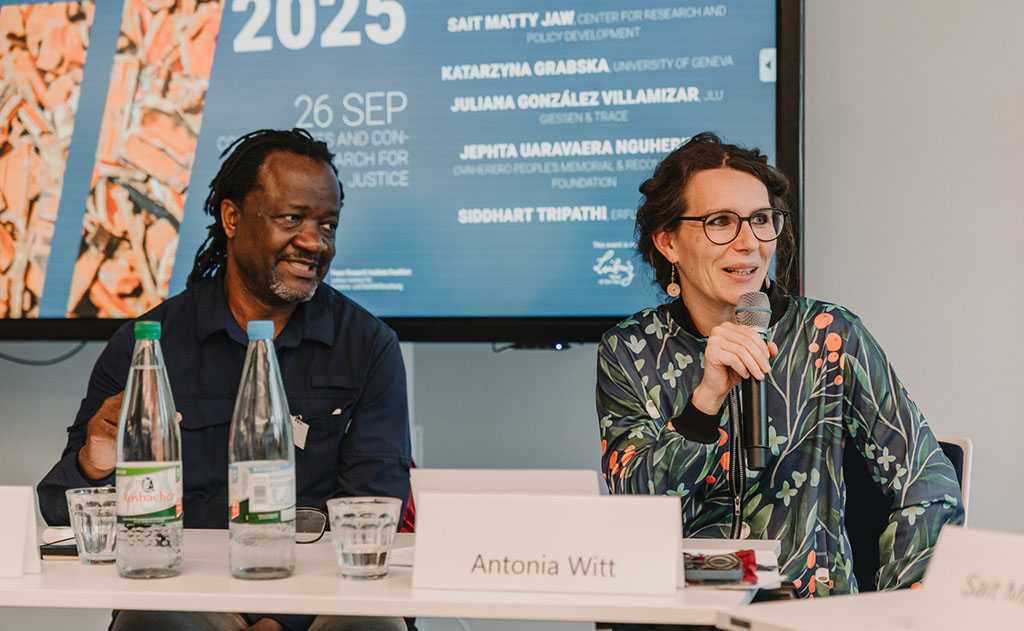 Zwei Personen sitzen auf einem Panel, eine Frau hält ein Mikrofon in der Hand.