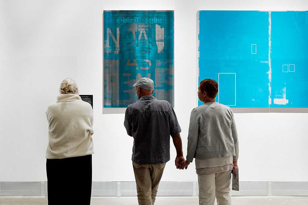 Drei Personen stehen vor zwei großen blauen Gemälden, zwei Personen halten sich an der Hand.