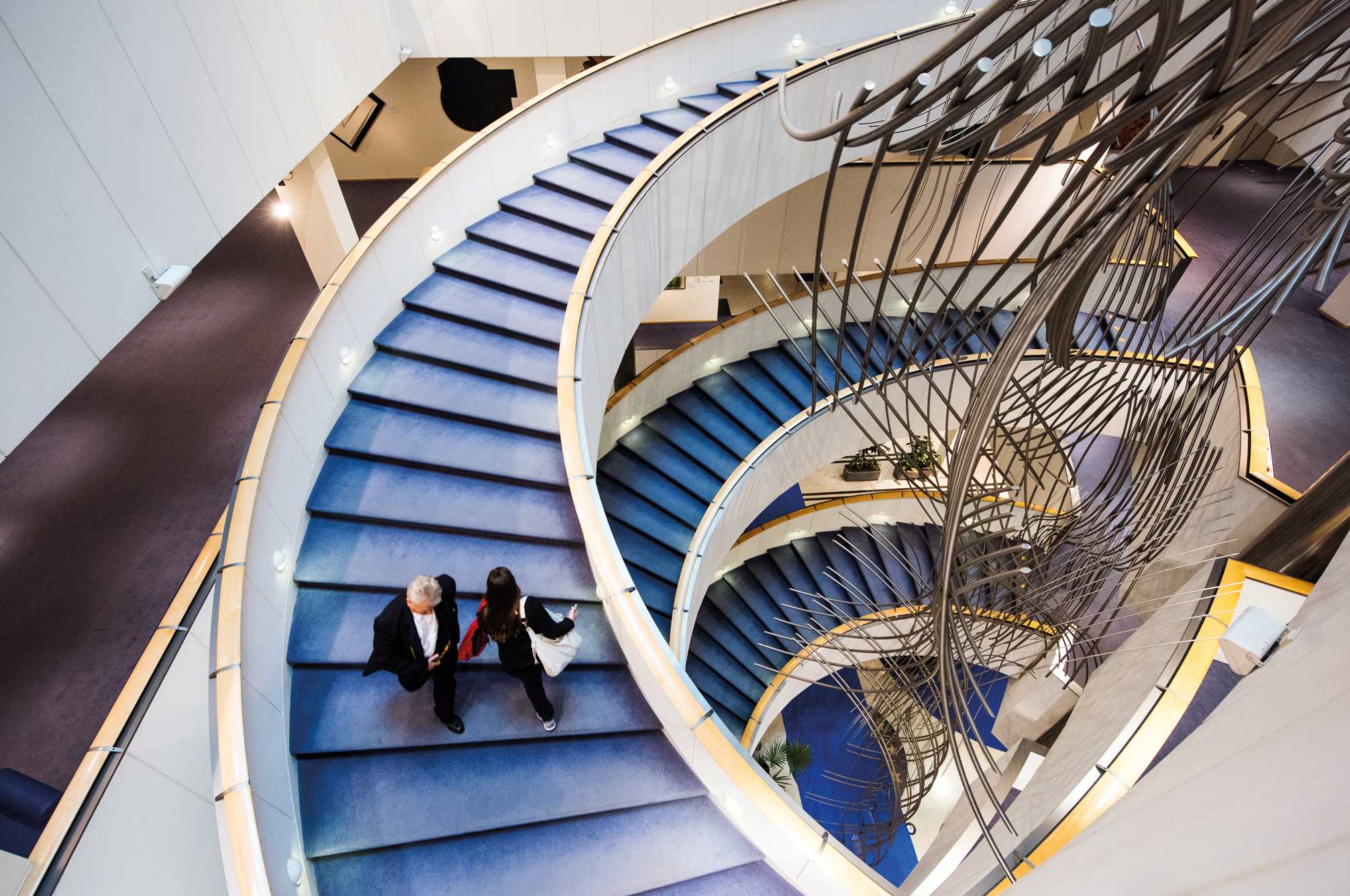 Auf einer blauen Wendeltreppe gehen zwei Personen.